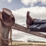 Cowboy,Boots,And,Hat,With,Feet,Up,On,Stables,Fence