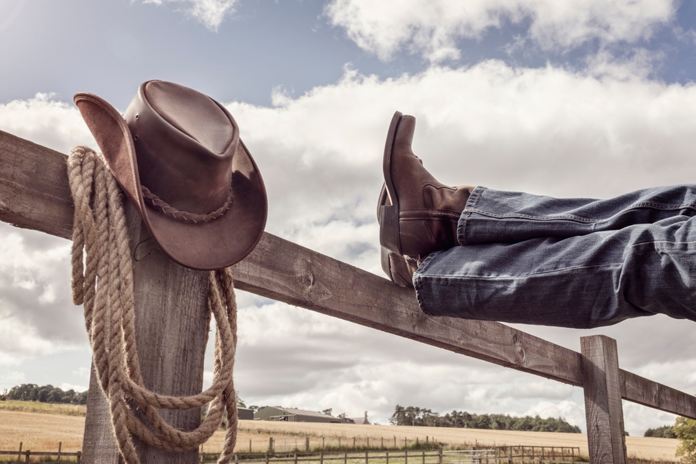 Cowboy,Boots,And,Hat,With,Feet,Up,On,Stables,Fence